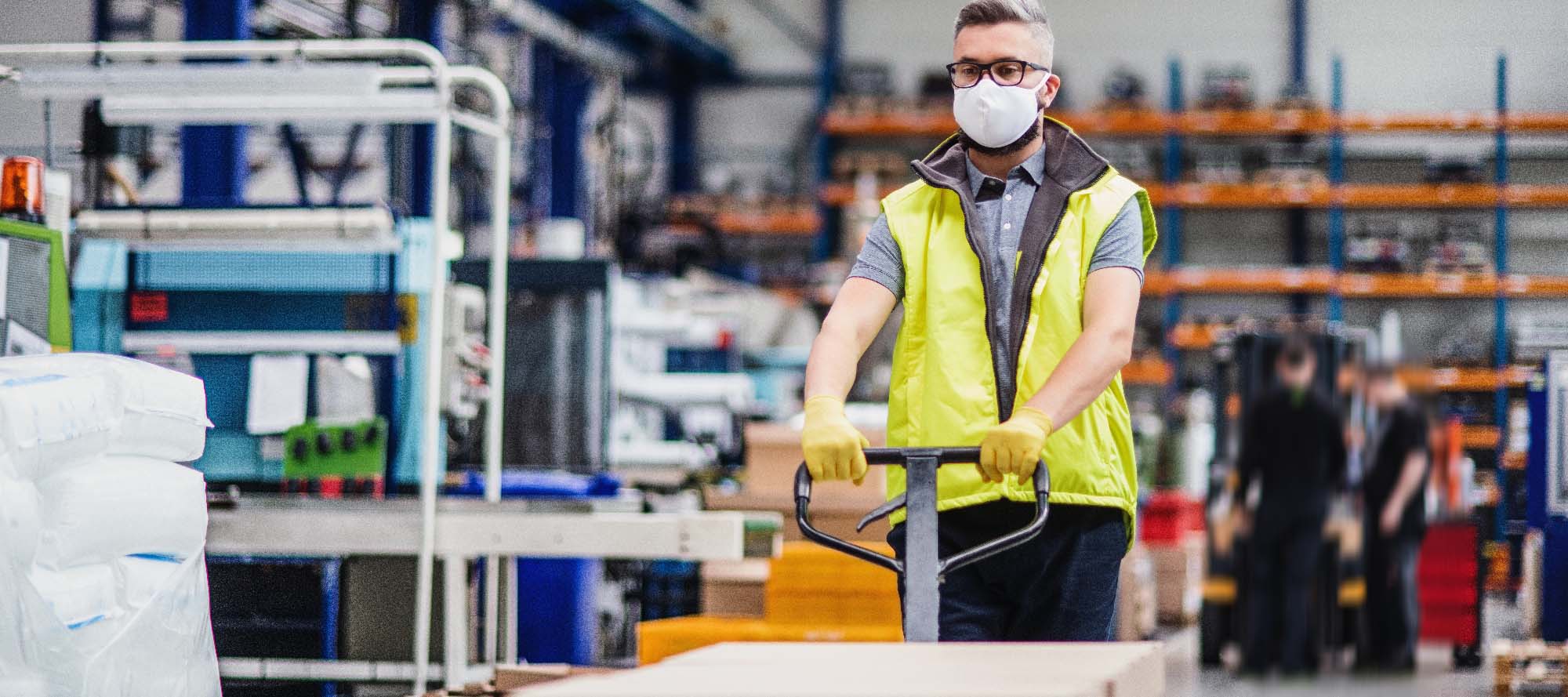 Male warehouse employee moving inventory while wearing a medical mask