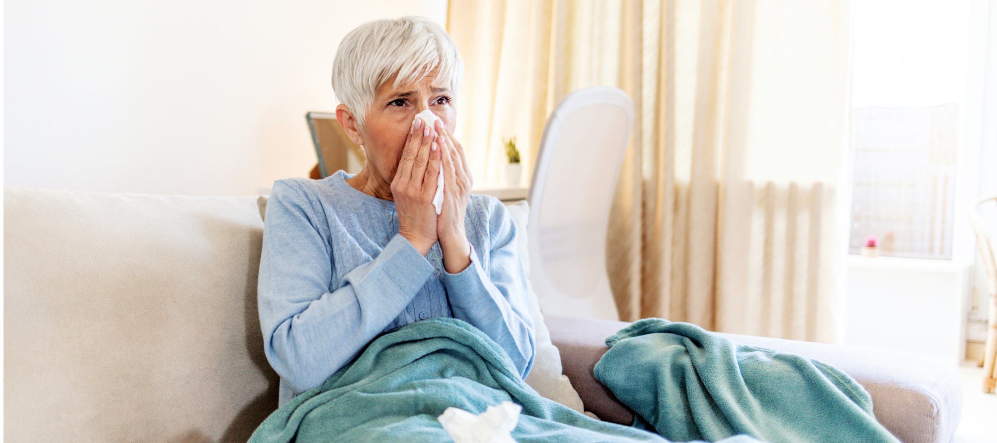 Shot of a senior woman blowing her nose with a tissue at home.