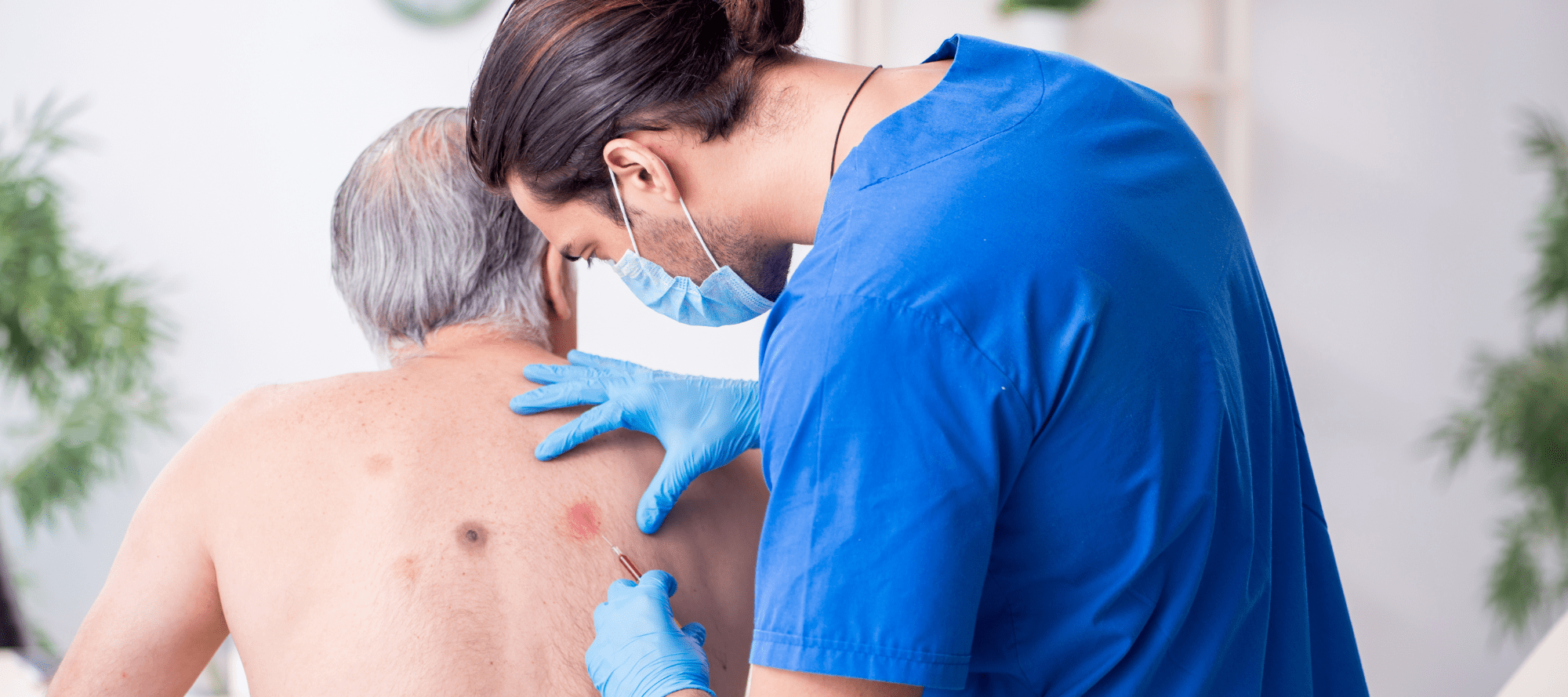 Mature man with red patches on back visiting a dermatologist that is inspecting skin