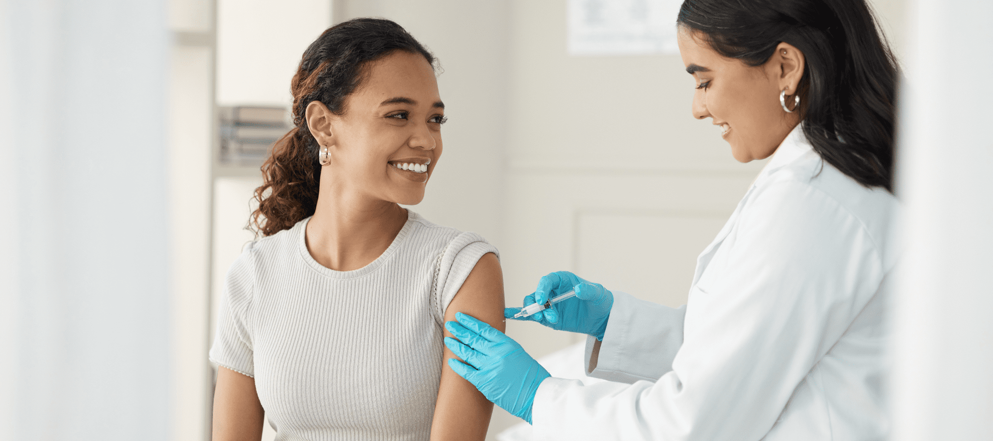 Young woman smiling with her sleeve rolled up as she gets an injection from a doctor on her upper arm