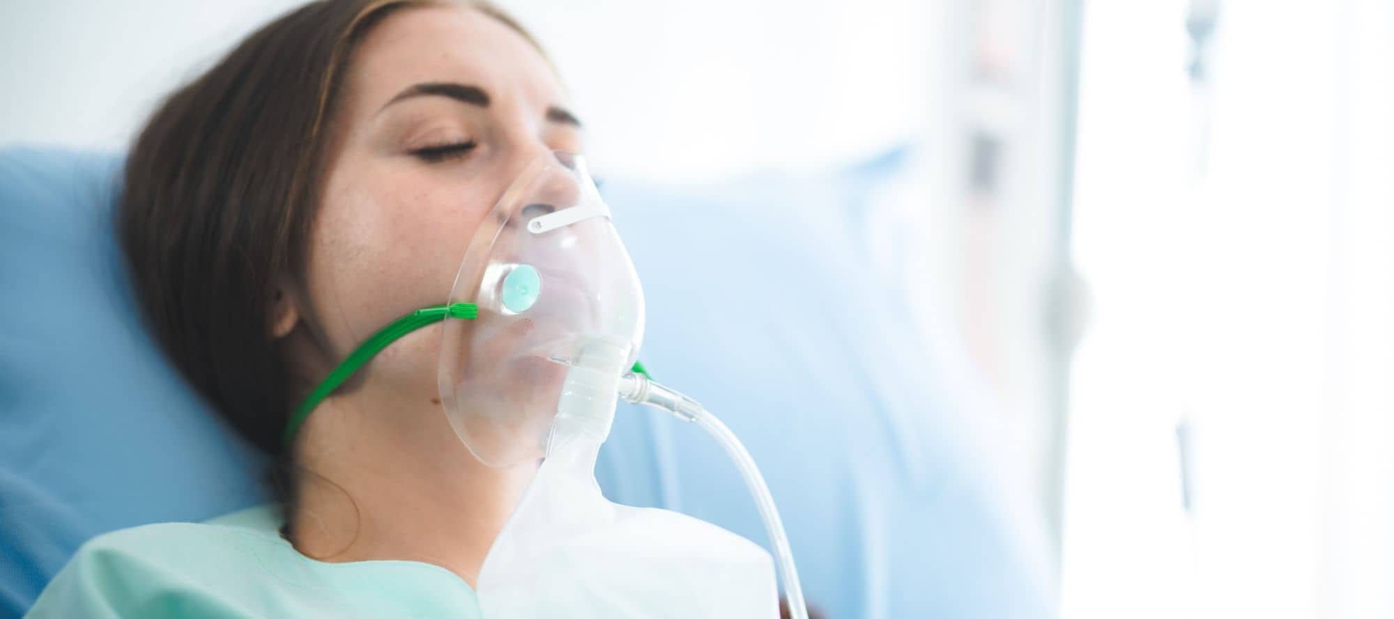 Young female patient wearing oxygen mask in hospital bed with her eyes closed
