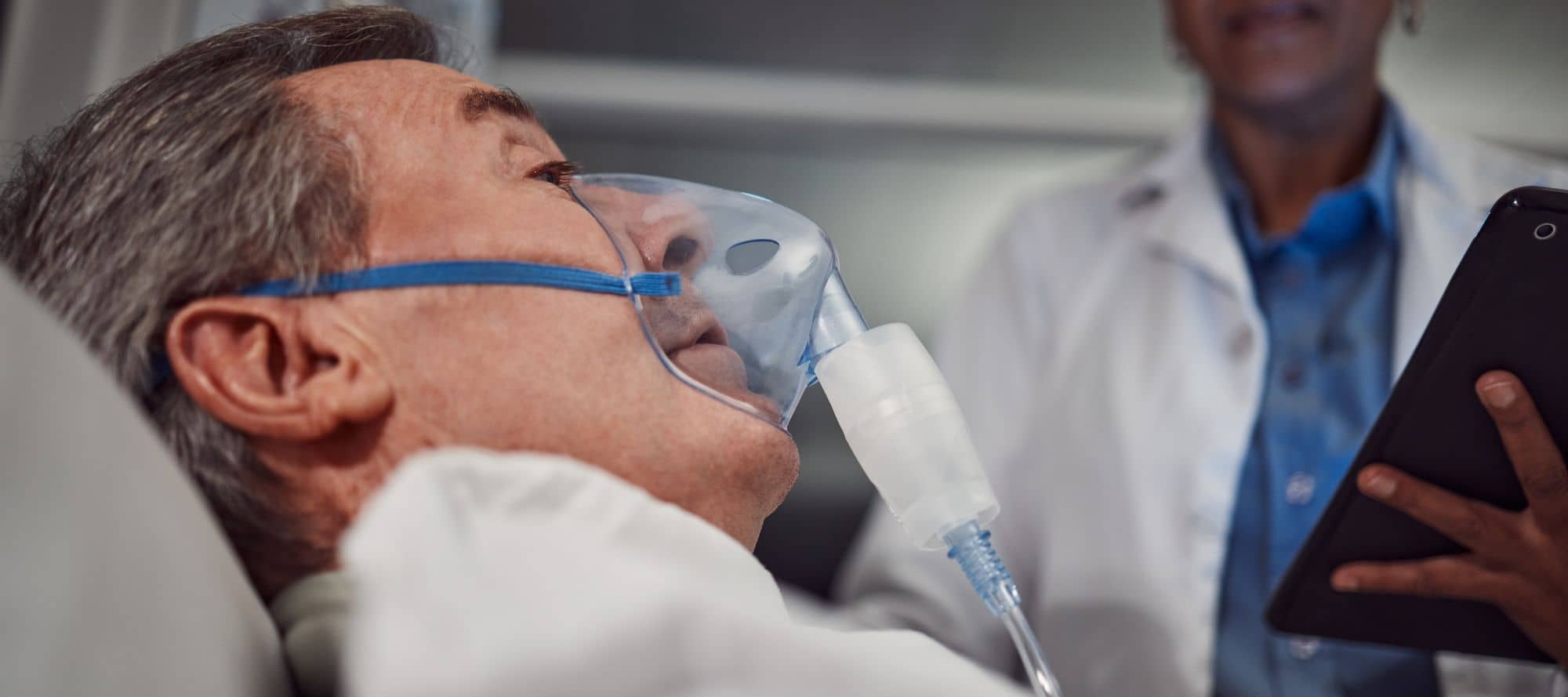 Senior man in the hospital with oxygen mask on speaking with doctor