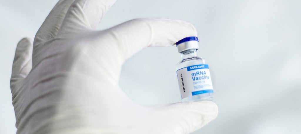Person wearing latex gloves holding onto bottle that reads "mRNA Vaccine COVID-19"