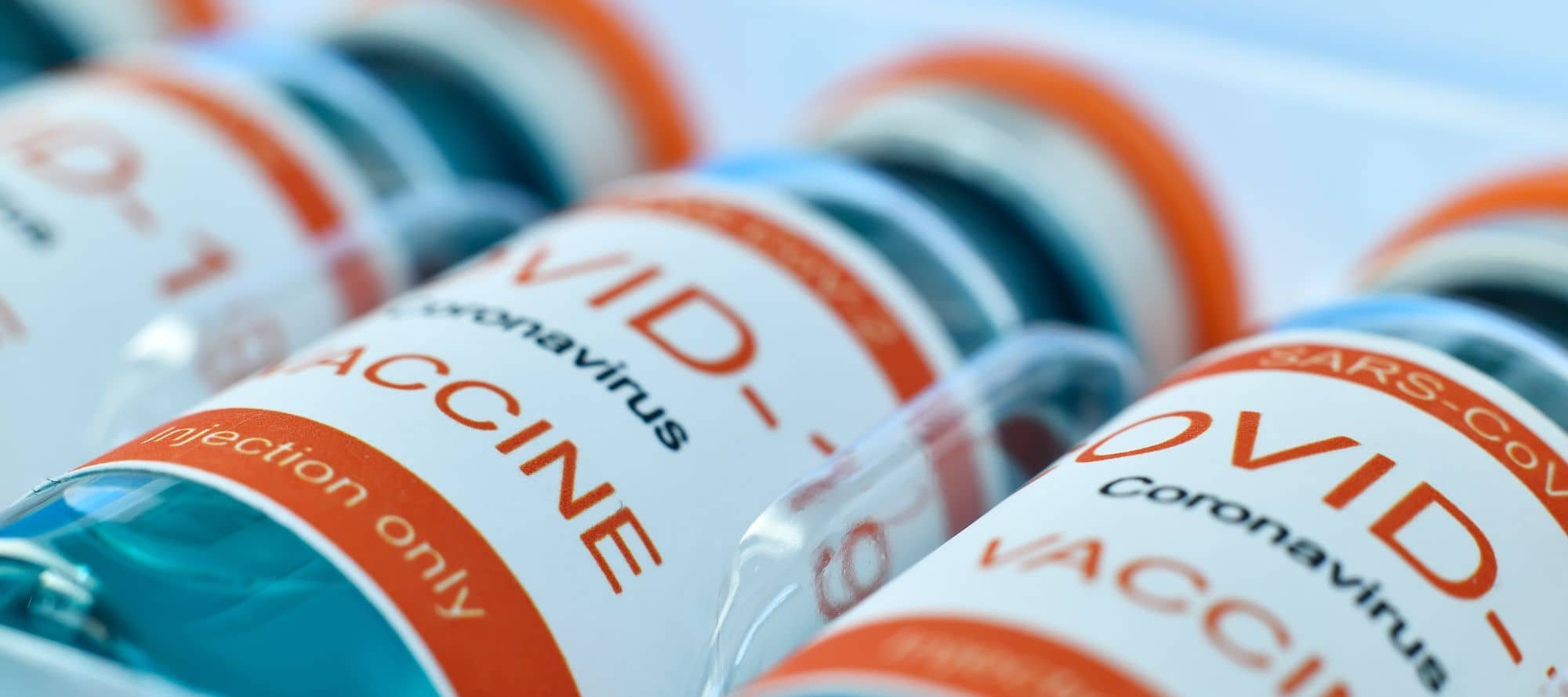 Vials lined up with white and orange branding and wording that signifies it is COVID vaccine