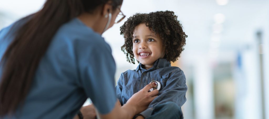 A young curly haired child smiling as doctor places stethoscope on his chest over his heart
